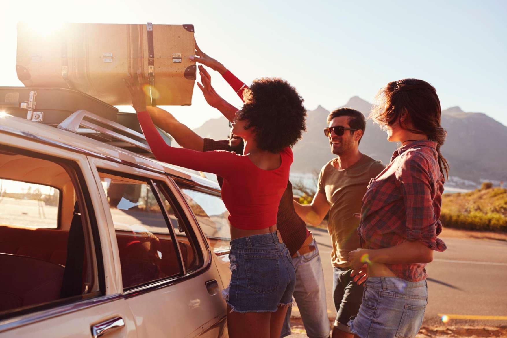 Friends strapping a suitcase to a car roof at sunset